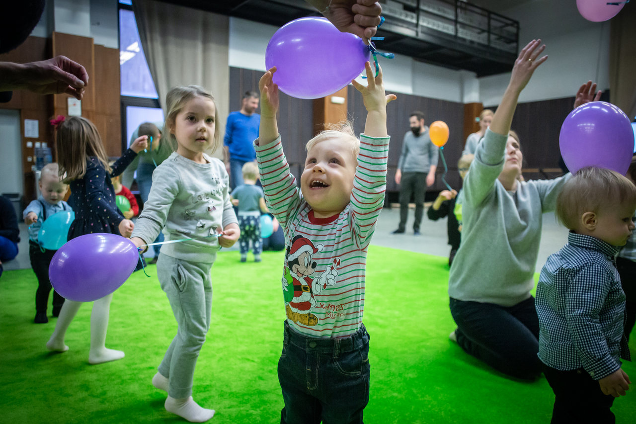 Grupa dzieci na zielonym dywanie bawi się balonami